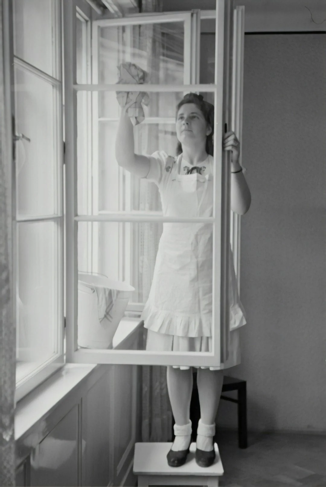 Close-up of hand cleaning window with squeegee outdoors using yellow gloves.